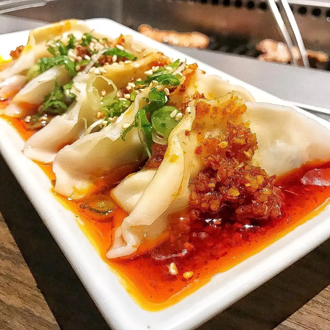 Steamed chicken dumplings topped with red chili, green onions, and sesame seeds.